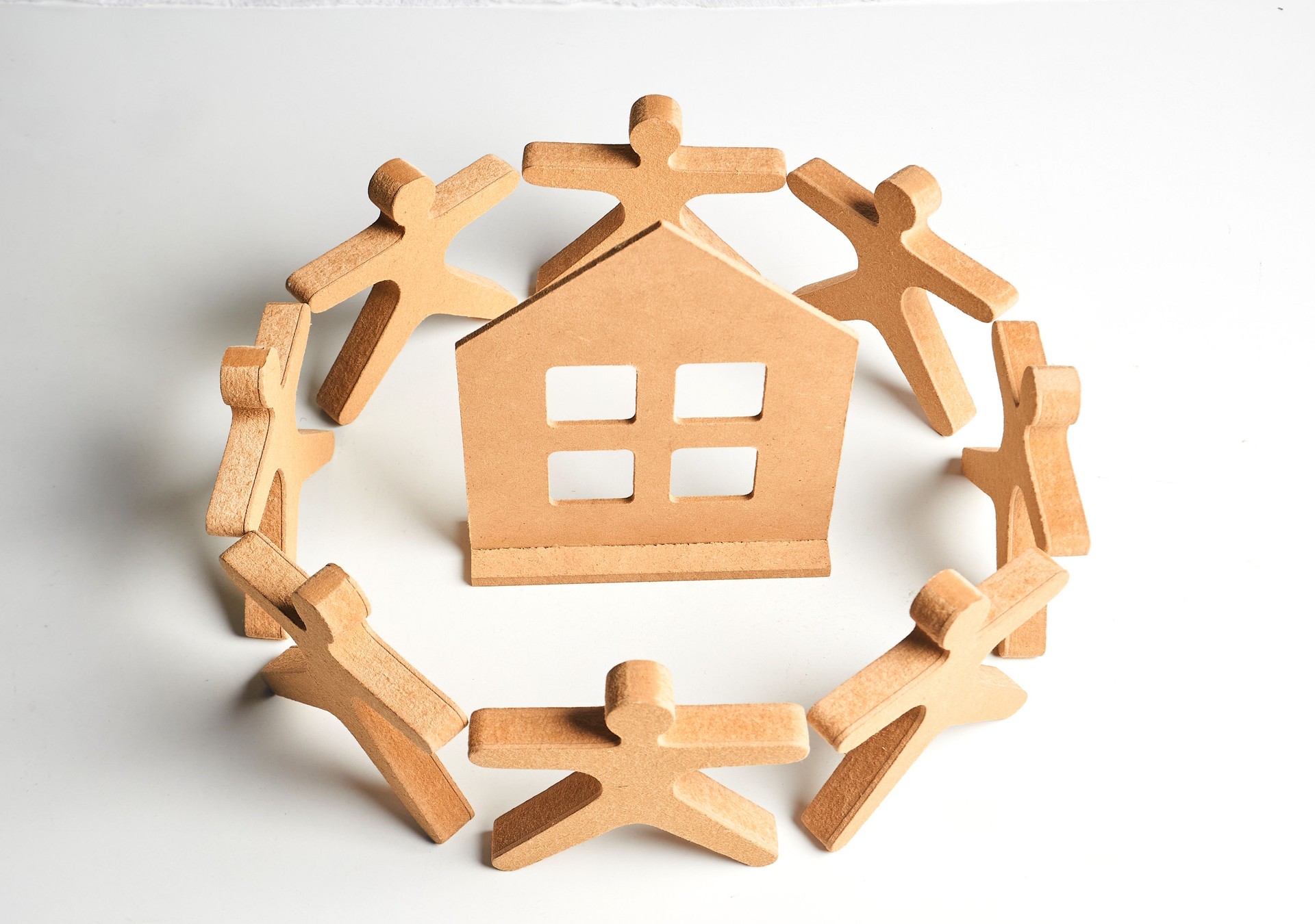 Wooden figures forming a protective circle around a house, symbolizing neighborhood support, safe housing and community care.